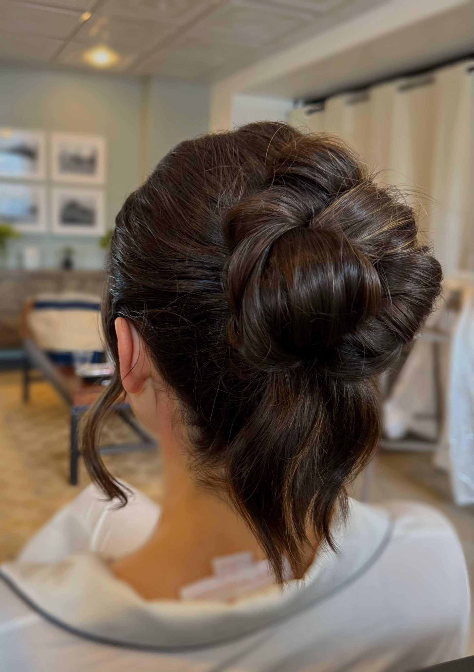 A woman with an elegant updo hairstyle featuring a twisted bun with loose strands in a cozy room.